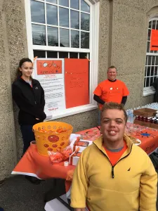 A smiling team member in a yellow jacket at the Today's Special table, with volunteers behind him
