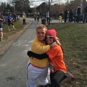 A team member in a yellow jacket hugging a runner in an orange shirt along the race course