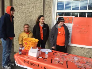 Team members and volunteers in orange shirts at the Today's Special table outside a brick building