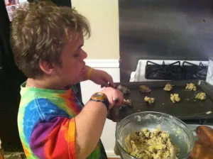 A team member in a tie-dye shirt scooping cookie dough onto a baking sheet