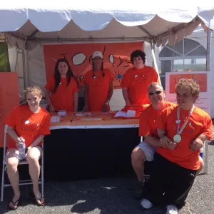 The Today's Special team in orange shirts at their booth under a white tent, two of them wearing medals