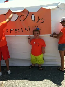 A smiling team member in an orange shirt standing in front of the hand-painted Today's Special banner