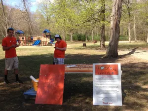 Two volunteers in orange shirts setting up the Today's Special table in a wooded park
