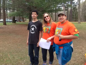 Three walkers smiling in a park, two wearing bright Best Buddies shirts