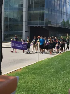 Walkers carrying a purple Best Buddies banner past a glass office building
