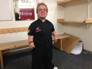 A young chef in a black chef's jacket posing in a stadium locker room