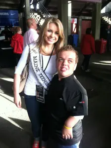 A young chef in a black jacket with a smiling pageant winner wearing a sash