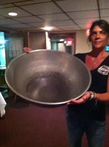 A smiling woman holding a large metal mixing bowl
