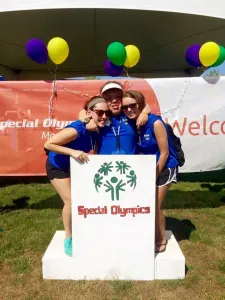 Two smiling volunteers in blue shirts posing with the Special Olympics podium
